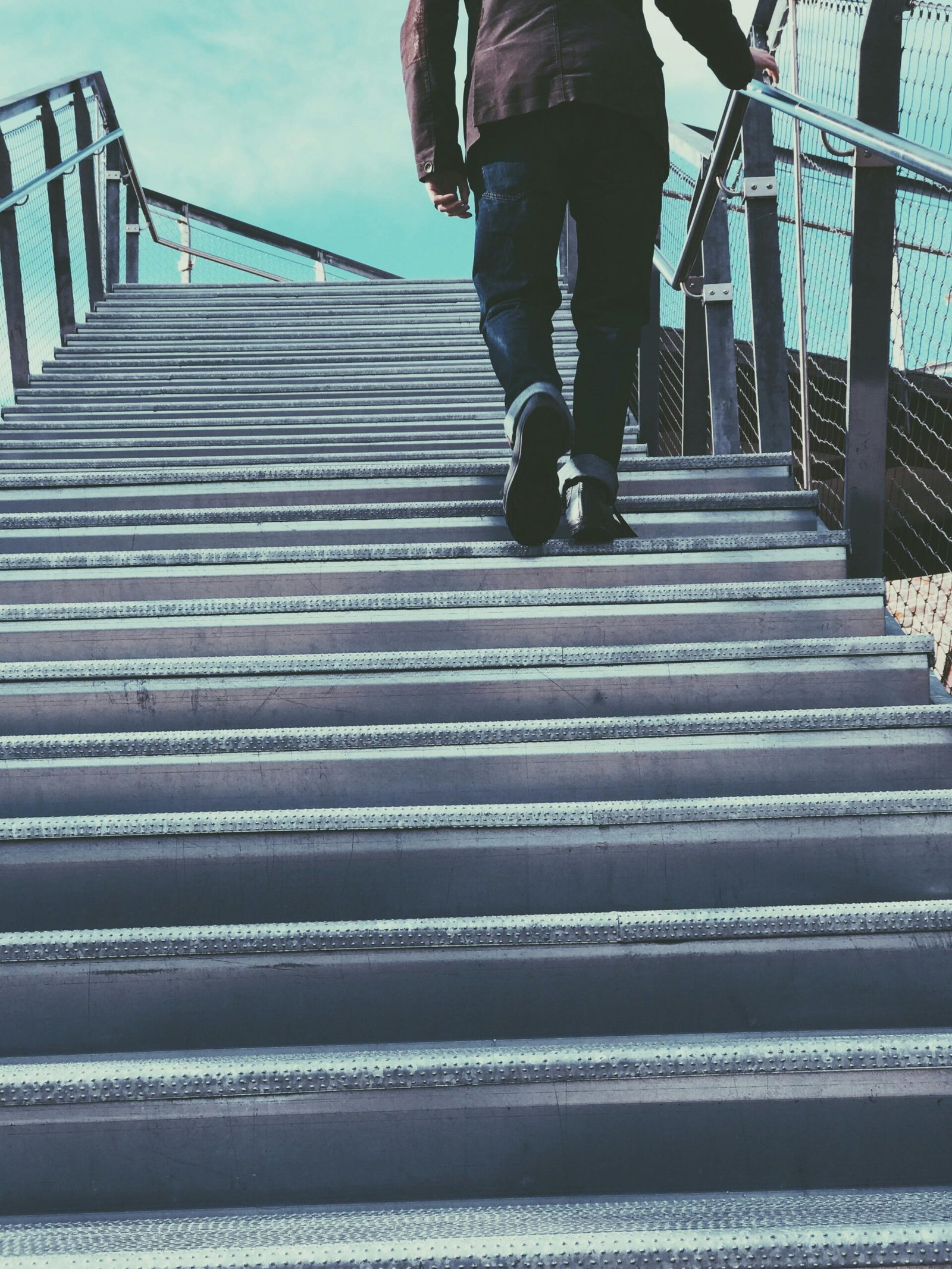 A person in casual wear ascends a metal staircase in an urban setting, suggesting travel or progress.